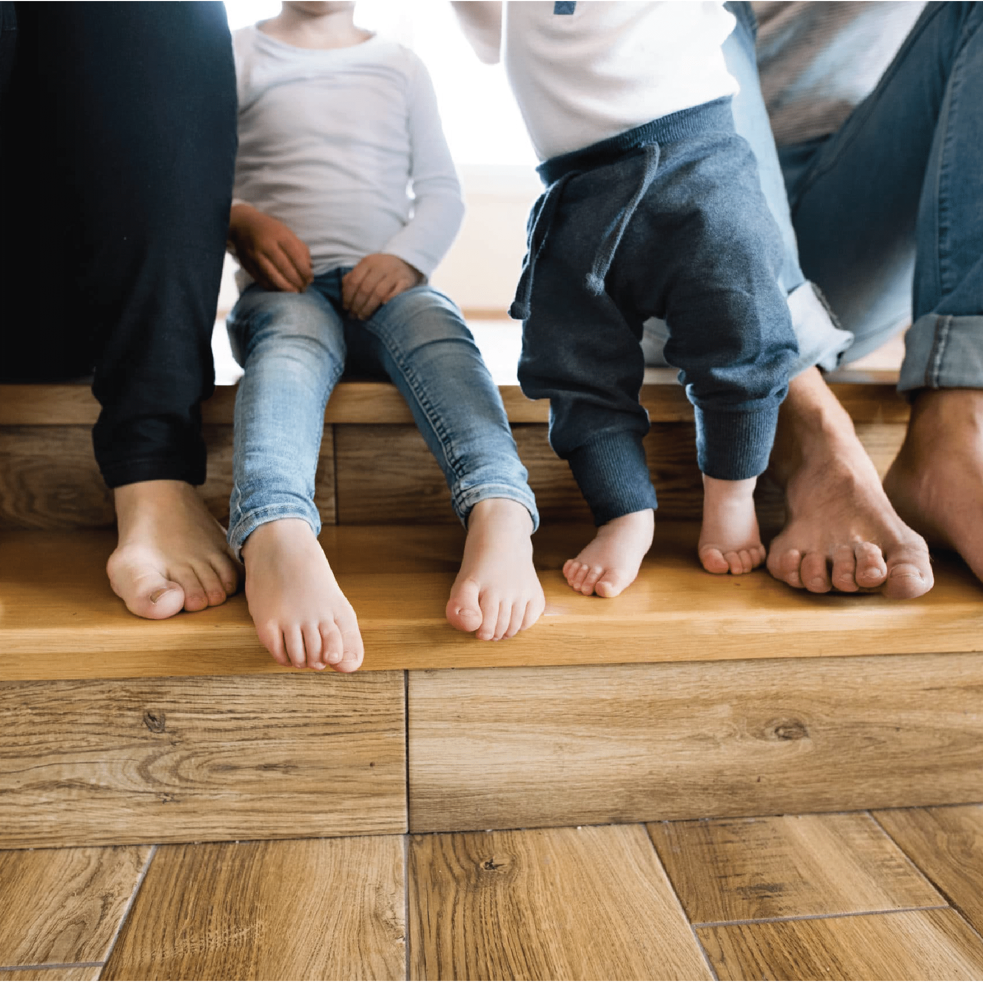 A family sitting on steps, barefoot on new hardwood floors - call Footprints Floors today to learn more about the home imrovement industry.
