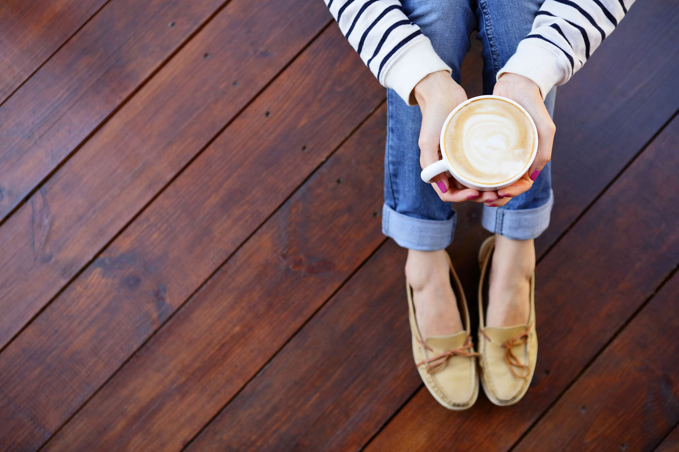 A person carefully drinking a hot drink sitting on hardwood floor.